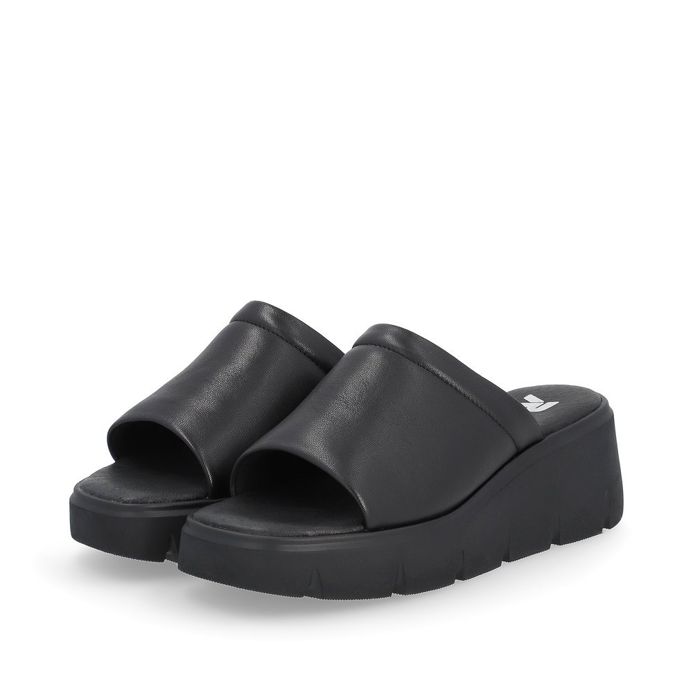 Black Rieker women´s mules W1551-00 with a flexible sole with wedge heel. Shoes laterally.