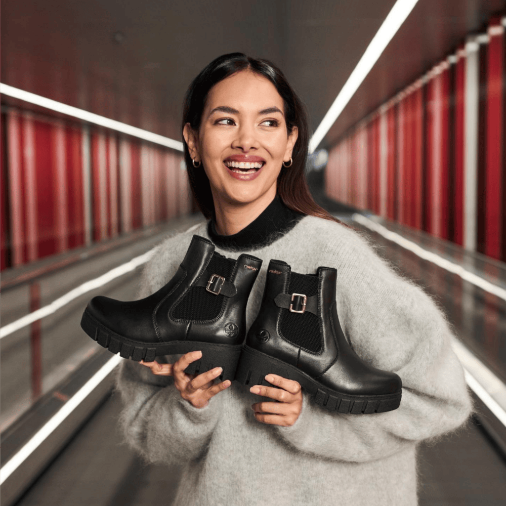 La femme tient des chelsea boots 74560-00 de Rieker.