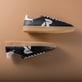 Schwarzer Rieker Herren Sneaker Low U2200-00 mit Schnürung sowie abriebfester Sohle. Schuhpaar seitlich liegend auf braunem Hintergrund.