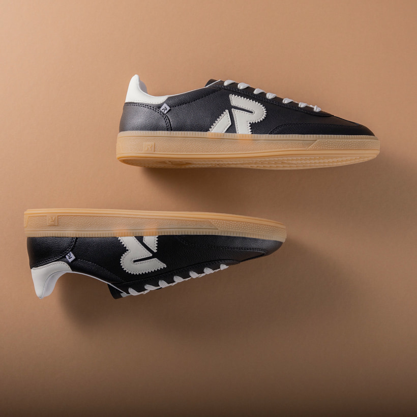Schwarzer Rieker Herren Sneaker Low U2200-00 mit Schnürung sowie abriebfester Sohle. Schuhpaar seitlich liegend auf braunem Hintergrund.
