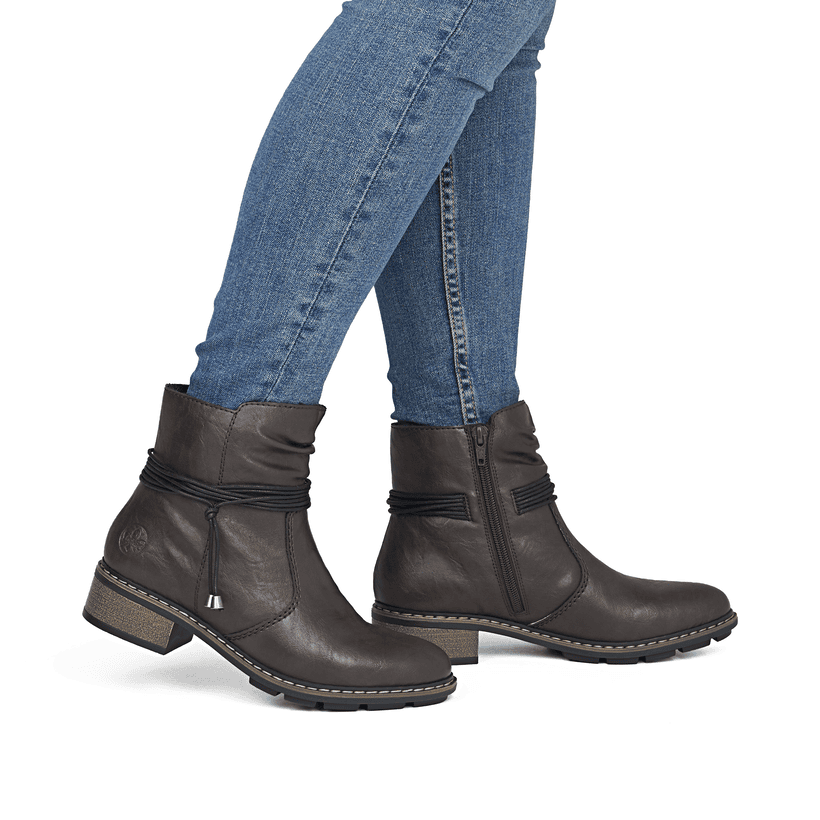 Dunkelbraune Rieker Damen Stiefeletten 77263-25 mit dekorativer Kordel. Schuh am Fuß.
