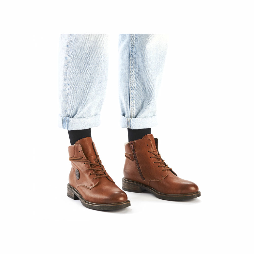 Braune Rieker Damen Schnürstiefel 71440-25 mit rundem Logo sowie Reißverschluss. Schuh am Fuß.