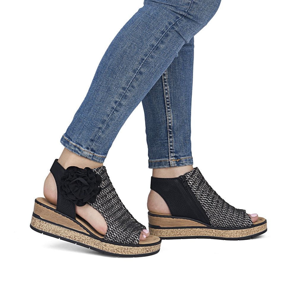 Schwarze Rieker Keilsandaletten 63791-01 mit dekorativer Blume. Schuh am Fuß.