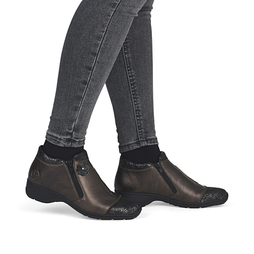 Braune Rieker Damen Kurzstiefel 58388-25 aus Glattleder mit dekorativer Blume. Schuh am Fuß.