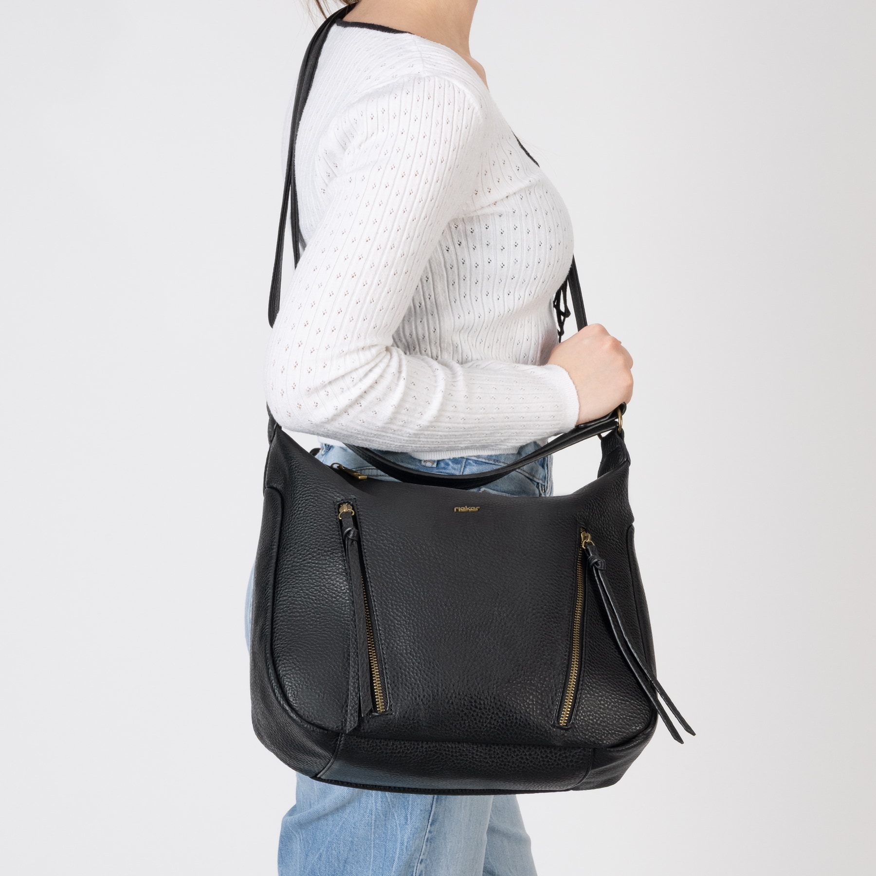Sac bandoulière Rieker H1016-00 en noir avec fermeture éclair ainsi que poches extérieures et intérieures. Porté.