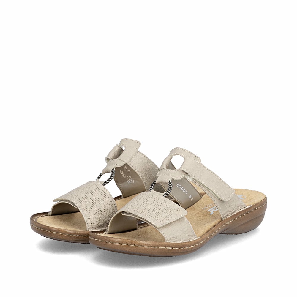 Beige Rieker Damen Pantoletten 60885-62 in Löcheroptik mit einem Klettverschluss. Schuhpaar seitlich schräg.