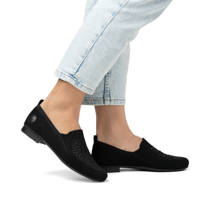 Schwarze Rieker Damen Slipper 51989-00 mit Strasssteinen sowie einem Gummizug. Schuh am Fuß.