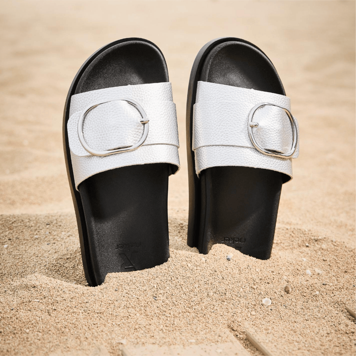 Les mules argentées W1453-90 pour femmes sont enfoncées dans le sable.